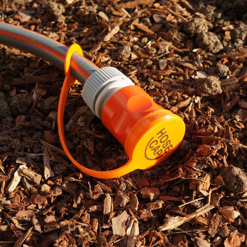 Orangefarbene HoseCap-Kappe auf der Kupplung eines Gartenschlauchs, am Schlauch eine Öse